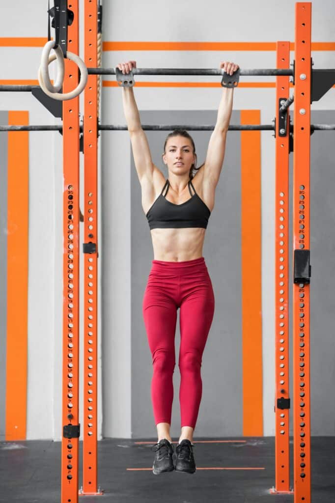 Fitte, sportliche Frau, die in einem Crossfit-Fitnessstudio einen Dead Hang macht