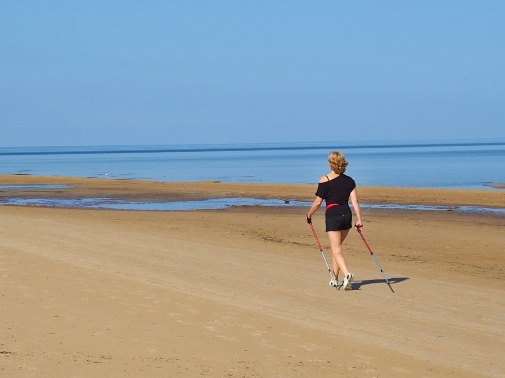 Junge Frau beim Nordic Walking am Ostseestrand um ihre Chronische Rückenschmerzen durch Laufen zu lindern 