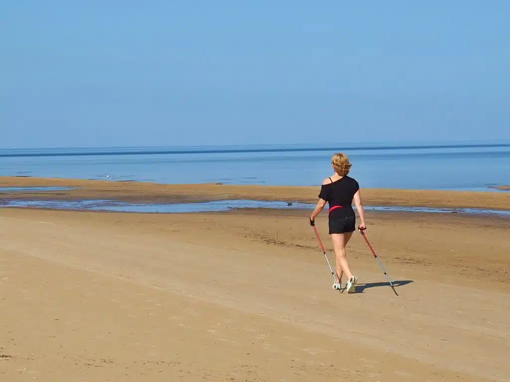 Junge Frau beim Nordic Walking am Ostseestrand um ihre Chronische Rückenschmerzen durch Laufen zu lindern 